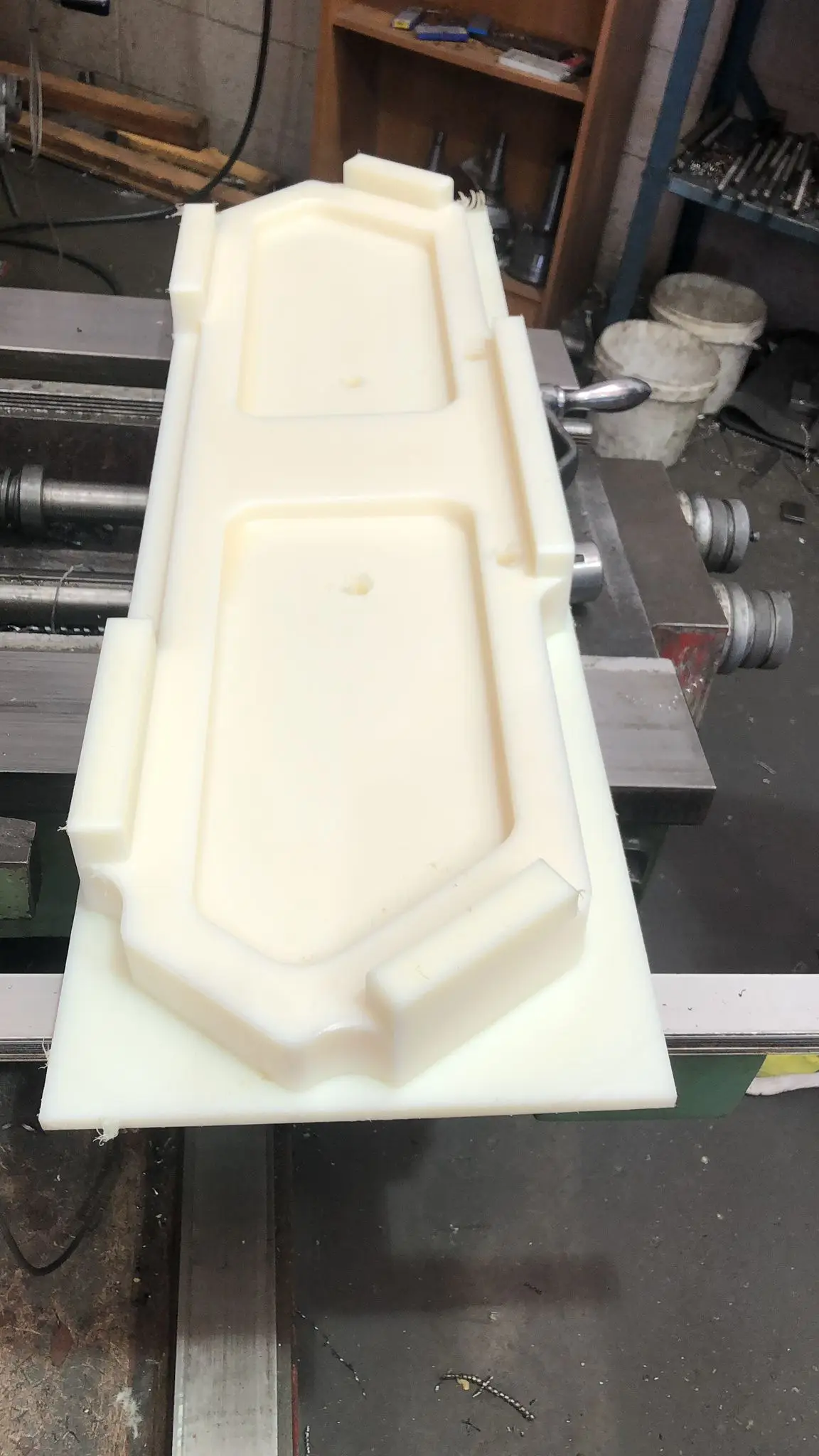 White engineering-plastic locator block, CNC milled, clamped on the machine table